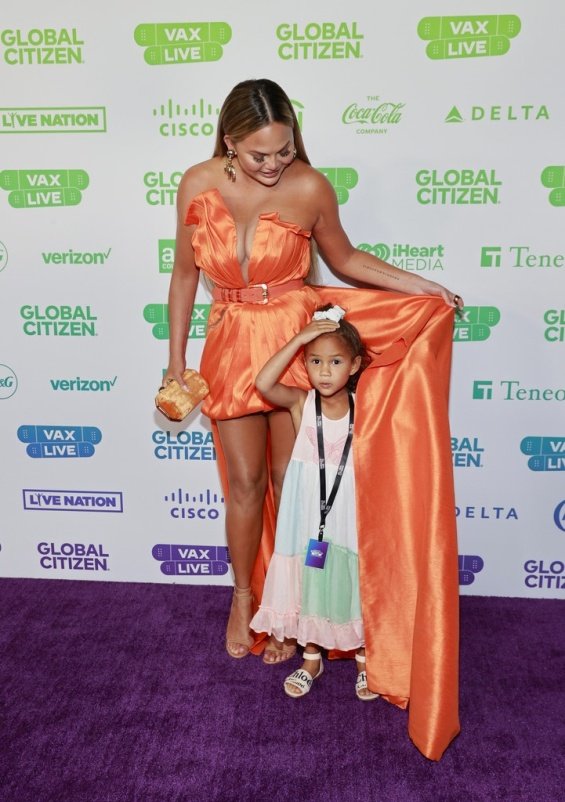 Chrissy Teigen in an orange creation at the Vax Live concert with her daughter Luna