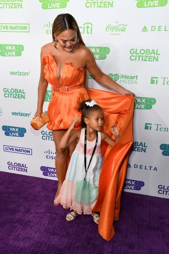 Chrissy Teigen in an orange creation at the Vax Live concert with her daughter Luna